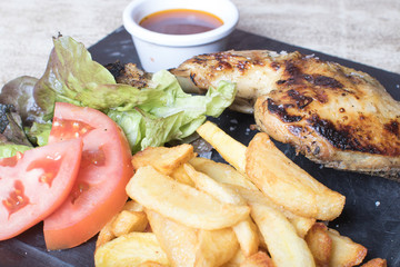 Chicken leg with potatoes, salad, tomato and sauce on black stone plate