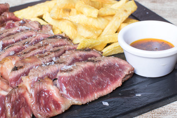 beef steak with potatoes and sauce on black stone plate