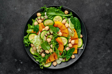 plate of pumpkin salad, avocado, cucumber, chickpeas, lettuce on a stone background.