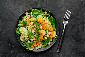 plate of pumpkin salad, avocado, cucumber, chickpeas, lettuce on a stone background.