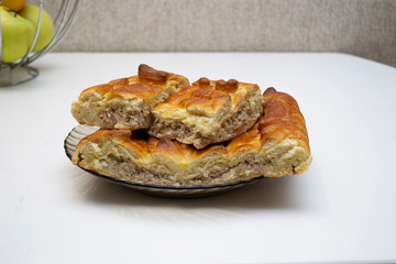 three pieces pie with meat on plate and white table in kitchen.