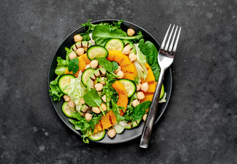 plate of pumpkin salad, avocado, cucumber, chickpeas, lettuce on a stone background.