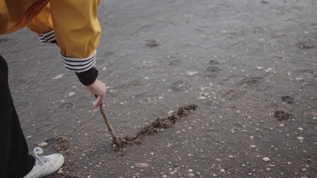Female in yellow raincoat on the beach writes I Love you in the sand using a stick