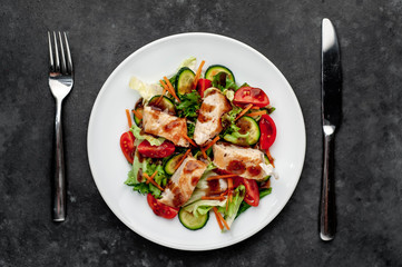 a plate of salad of tomato, chicken, cucumber, carrots, soy sauce in a plate on a stone background