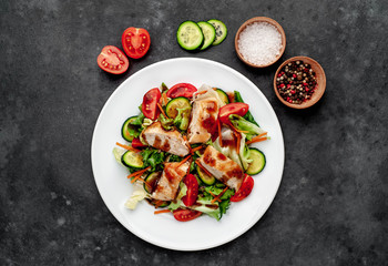 a plate of salad of tomato, chicken, cucumber, carrots, soy sauce in a plate on a stone background