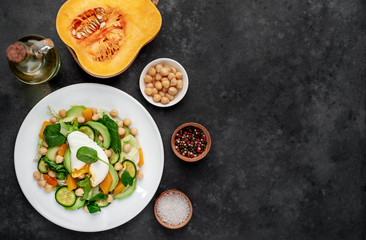 a plate of avocado salad, chickpeas, pumpkin, cucumber, poached egg in a plate on a stone background with copy space for your text
