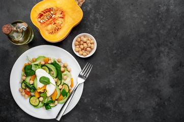 a plate of avocado salad, chickpeas, pumpkin, cucumber, poached egg in a plate on a stone background with copy space for your text