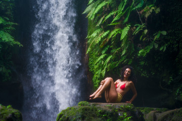 outdoors tropical lifestyle portrait of young attractive and happy hipster girl enjoying nature excited feeling free at amazing beautiful waterfall in exotic holidays travel