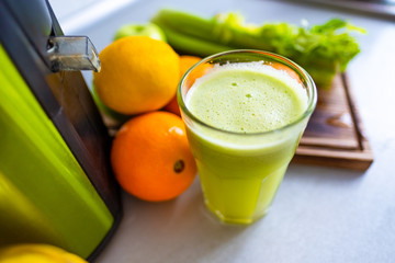 Freshly squeezed green juice in a glass on the table. Bright fruits on a wooden board apple, lemon, celery, orange.