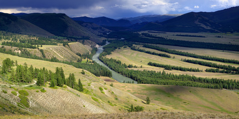 Mountain valley, above a river, panorama landscape, Altay. The contrast of the stormy sky and light in the valley.