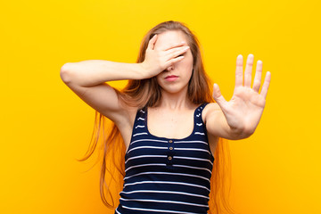 yound blonde woman covering face with hand and putting other hand up front to stop camera, refusing...