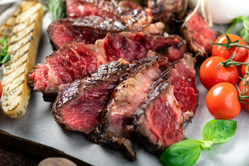 Sliced Tomahawk steak Grilled in Italian style with burata cheese, Basil and tomatoes on a wooden Board