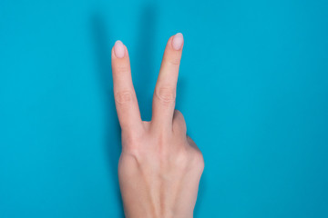 Beautiful female manicured hand isolated on blue background showing two fingers up.