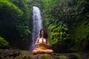 outdoors portrait of young attractive and happy hipster girl doing yoga at beautiful tropical waterfall meditating enjoying freedom and¡ nature in wellness and zen lifestyle