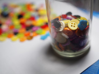 Closeup and focus cloth sewing buttons in glass bottle and blurred background.