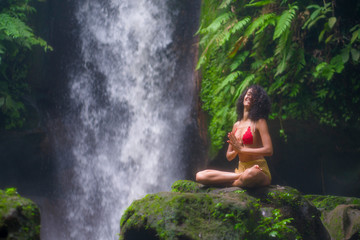 outdoors portrait of young attractive and happy hipster girl doing yoga at beautiful tropical waterfall meditating enjoying freedom and¡ nature in wellness and zen lifestyle