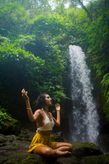 outdoors portrait of young attractive and happy hipster woman doing yoga at beautiful tropical waterfall meditating enjoying freedom and¡ nature in wellness and zen lifestyle