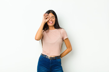 young pretty latin woman smiling happily with funny face, joking and looking through peephole,...
