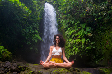 outdoors portrait of young attractive and happy hipster woman doing yoga at beautiful tropical waterfall meditating enjoying freedom and¡ nature in wellness and zen lifestyle