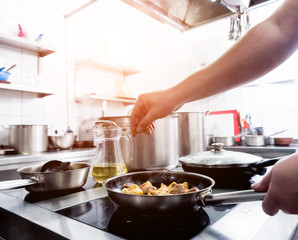 Chef cooks fried potatoes with pieces of meat in a restaurant kitchen