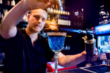 The bartender makes a cocktail with a fire show at the bar. Bartender at work. 