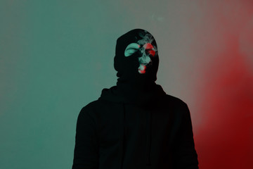 young man in hoodie and balaclava closing eyes and blowing smoke out