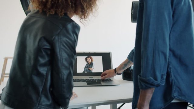 Back view slowmotion of man and woman watching photos on laptop screen in photography studio, Afro-American model is enjoying pictures after photoshoot.
