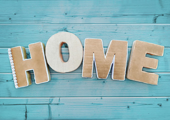 Volume letters "Home" made of cardboard on a blue wooden table. Background for design with copy space for your text.