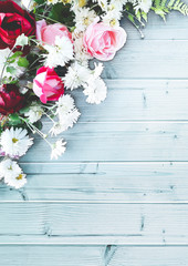 Beautiful vertical decorative composition of flowers on a blue wooden table. Top view, background with copy space for your text. Red and pink roses, white daisies.