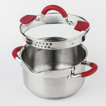 Stainless casserole with glass lid and red handles on grey background.