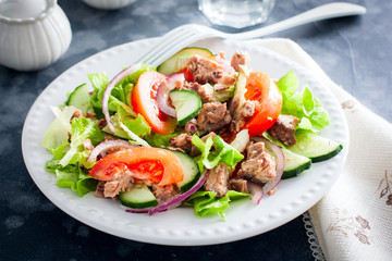 Salad with tuna and fresh tomatoes, cucumber and onions, on a white plate, selective focus