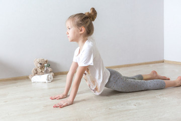 A little cute girl practices a yoga pose indoors. The child does yoga and gymnastic exercises.