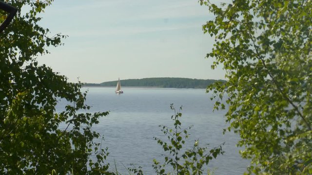 The smoke of the fire. Refraction image. View of the river through the green trees. Bright summer day. Far sailing boat