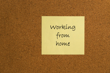 Small yellow sticky note on an office cork bulletin board with the message working from home