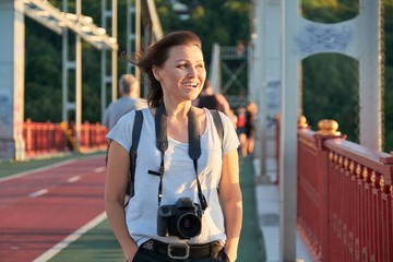 Mature female with backpack photo camera smiling on sunny summer day