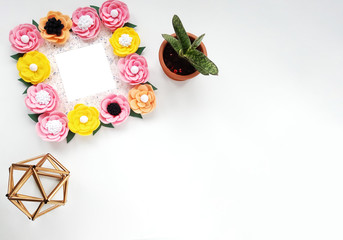 Decorative frame with colorful felt flowers and leaves, a golden geometric figure and a houseplant. Top view, background with copy space for your text on a white background.