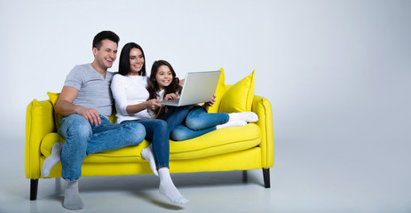Best day ever. Married couple and their little daughter taking rest at home, sitting on a couch and watching movies on their laptop.