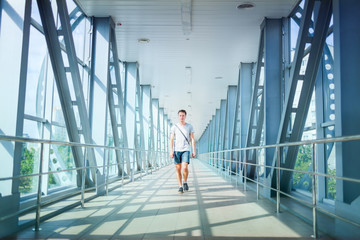 Front view of handsome gentleman strolling over big bridge. Good-looking guy wearing t-shirt and denim shorts while taking walk. Concept of man in city.