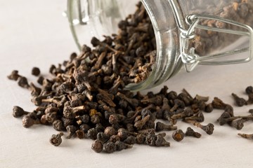 Heap of raw, dried cinnamon blossom buds spice in glass storage jar on white table background