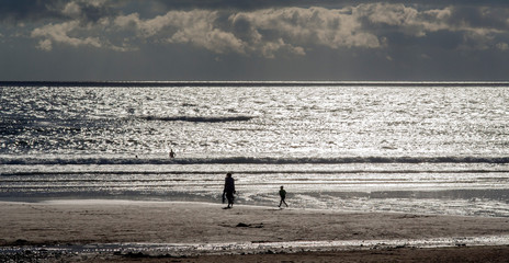 Fototapeta na wymiar Silhouettes of people at beach, including young child.