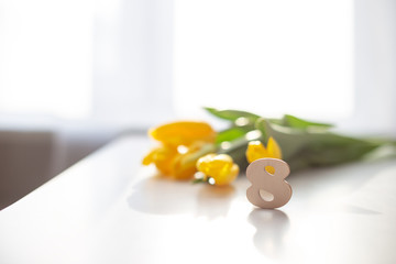 Wooden number eight and bouquet of yelow tulips stands on a white table.