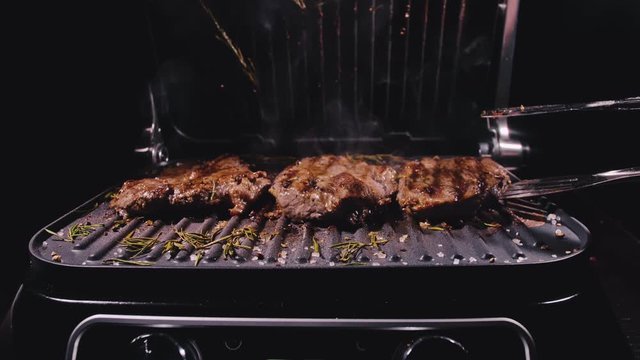 Delicious juicy meat steak cooking on grill. Kitchen tongs. Aged prime rare roast grilling tenderloin fresh marble tenderness beef. Prime beef fry on electric roaster, rosemary black pepper, salt.