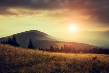 Beautiful landscape in the mountains at sunrise with haze and cloudy sky. View of the magnificent natural scenery of mountains hills. Filtered image: cross processed retro effect.