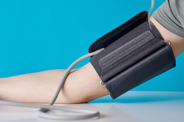 Woman measuring blood pressure with a digital pressure monitor against blue background. Health care...