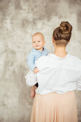 Young beautiful mother holding her little toddler son in hands and smiling. Happy loving family. Concept of care, love and protection