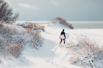 Cold winter and surfer with surfboard. Snowy day with surfer in wetsuit.