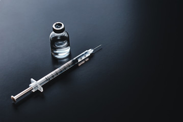 Medical syringe and ampoule with medicine on the black background, top view with copy space....
