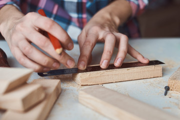 Carpenter hands taking measurement with a pencil of wooden plank. Concept of DIY woodwork and furniture making
