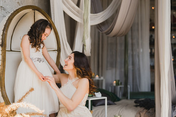 Mother and daughter hugging and playing together. Pretty little girl and beautiful woman. Girls in lace dresses playing in decorated room. Family weekend, beauty day, having fun, love concept.