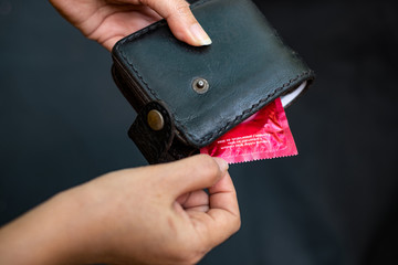 Closeup woman hand holding black Leather Wallet with a red condom at the black background